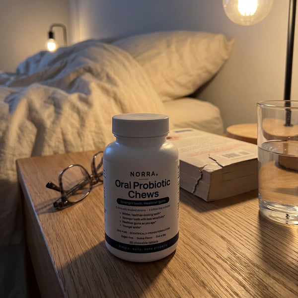 A bottle of Norra on a bedside table beside reading glasses and a book